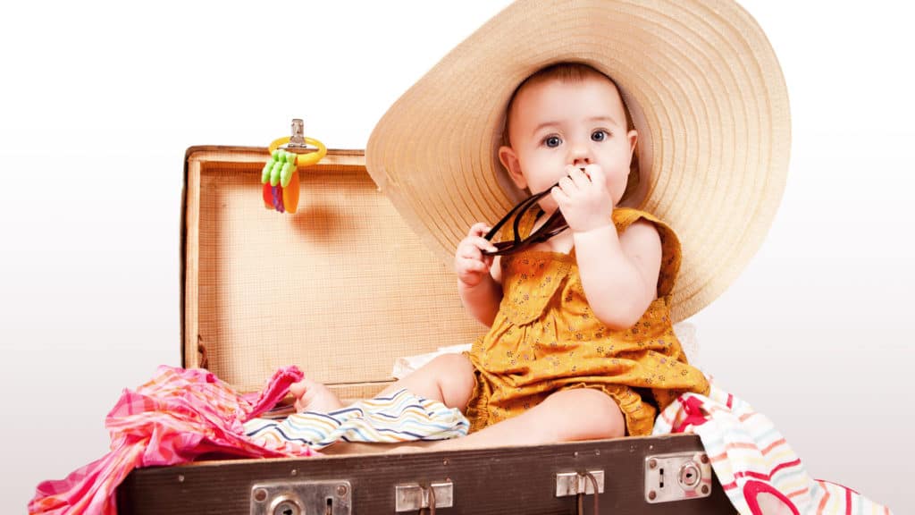 Cute baby with big summer sombrero sitting in an old suitcase ready to travel