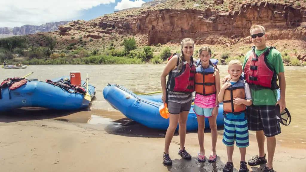 Family rafting on the Colorado River in Arizona with boats, river, and mountains in the background