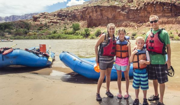 Family rafting on the Colorado River in Arizona with boats, river, and mountains in the background