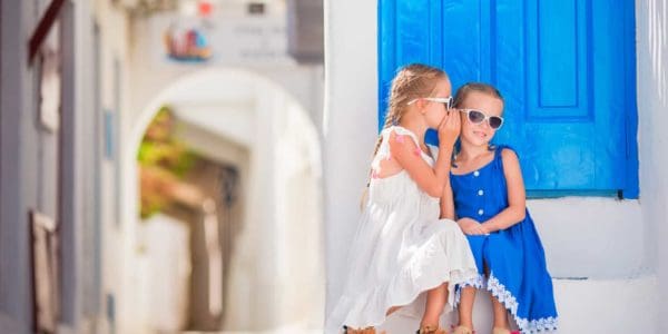 Little girls sitting in front of a typical house in a village in Mykonos, Greece