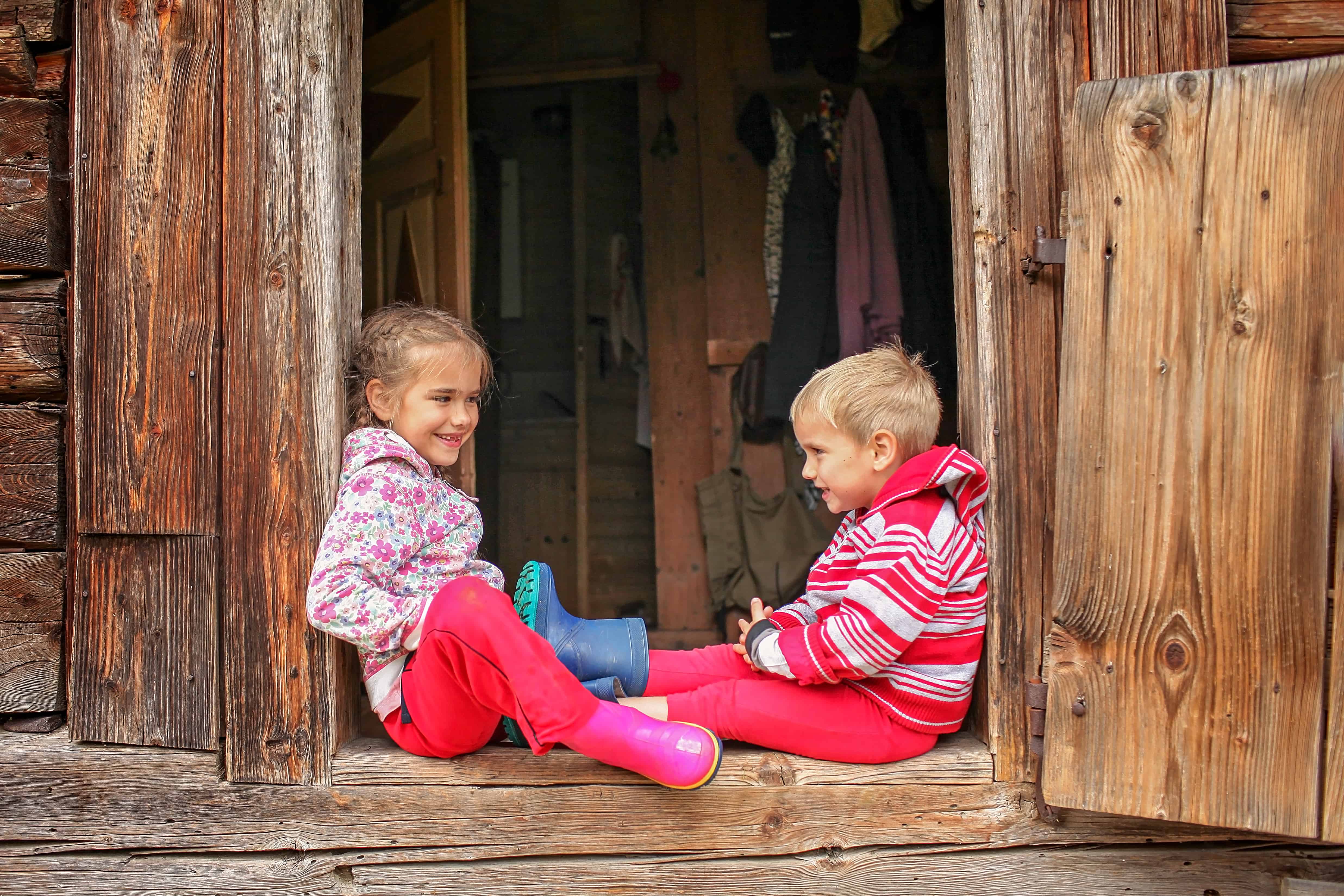 Boy and girls sitting in entrance of a wooden house during summer staycation