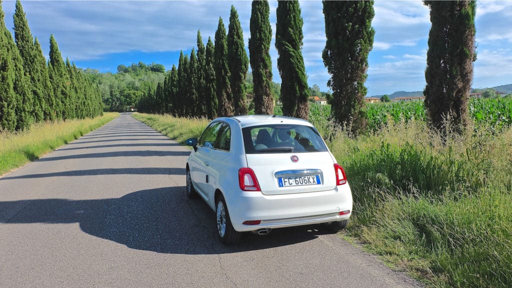 White Fiat 500 on a road trip in Tuscany Italy with typical landscape
