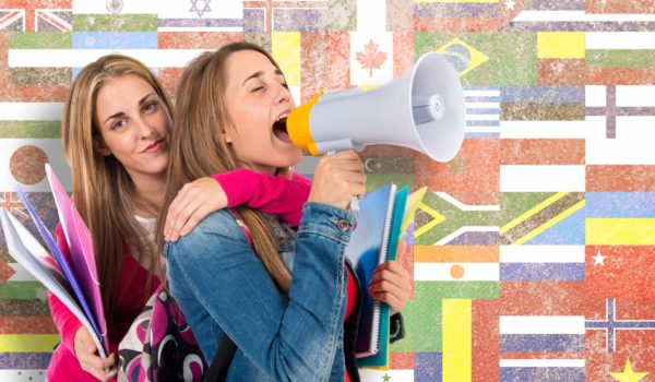 Two girls shouting by megaphone about learning new languages with flags in background