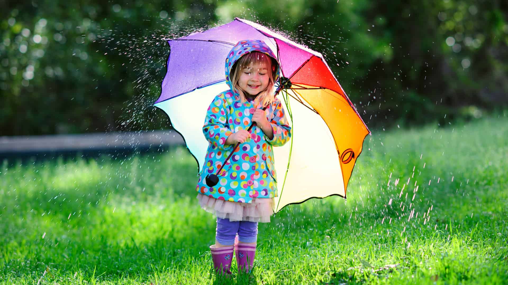 Cute girl standing in the rain under an umbrella in the grass