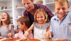Father cooking pizza with happy kids in a kitchen