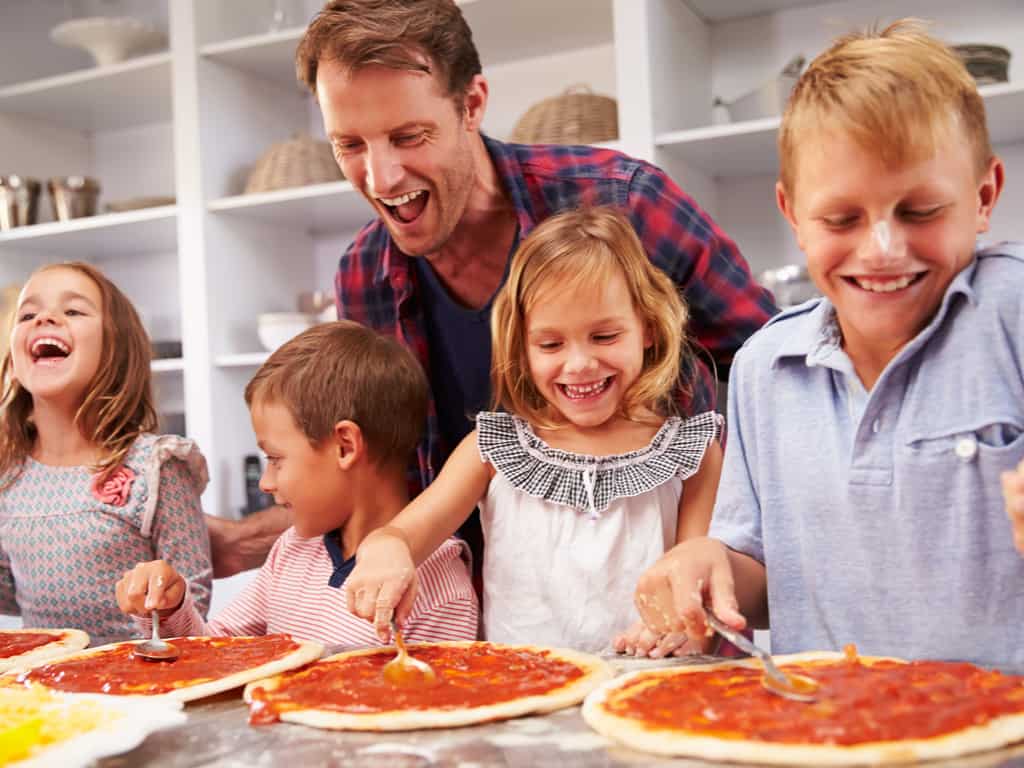 Father cooking pizza with happy kids in a kitchen