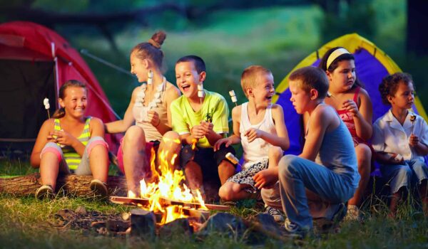 Kids sitting around an open fire while camping and eating marshmallows