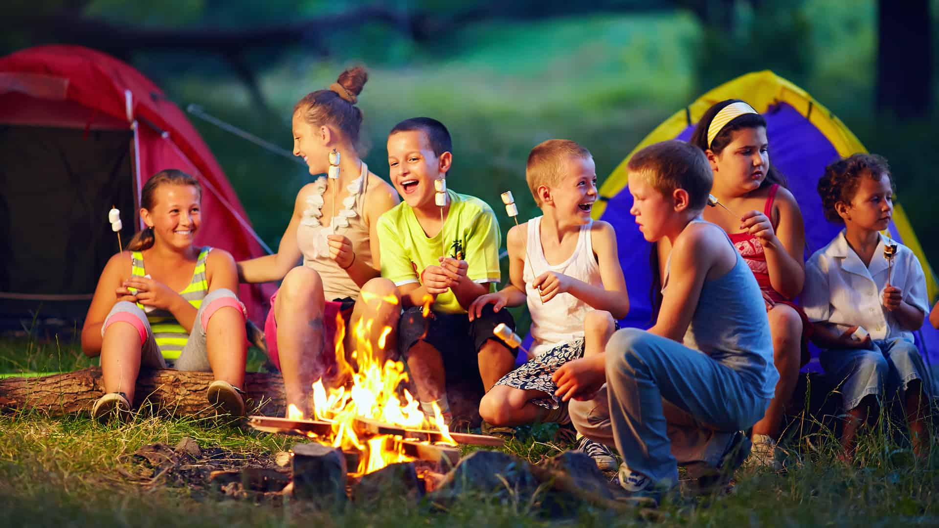 Kids sitting around an open fire while camping and eating marshmallows