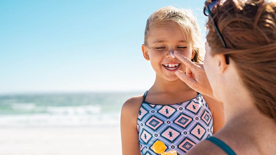 Mother applies sunscreen on her daughter's nose and face