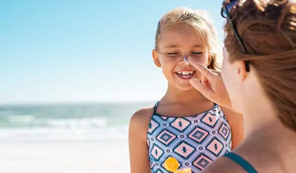 Mother applies sunscreen on her daughter's nose and face