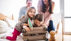 Parents with two kids over a suitcase getting them ready for a trip abroad