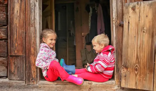 Boy and girls sitting in entrance of a wooden house during summer staycation